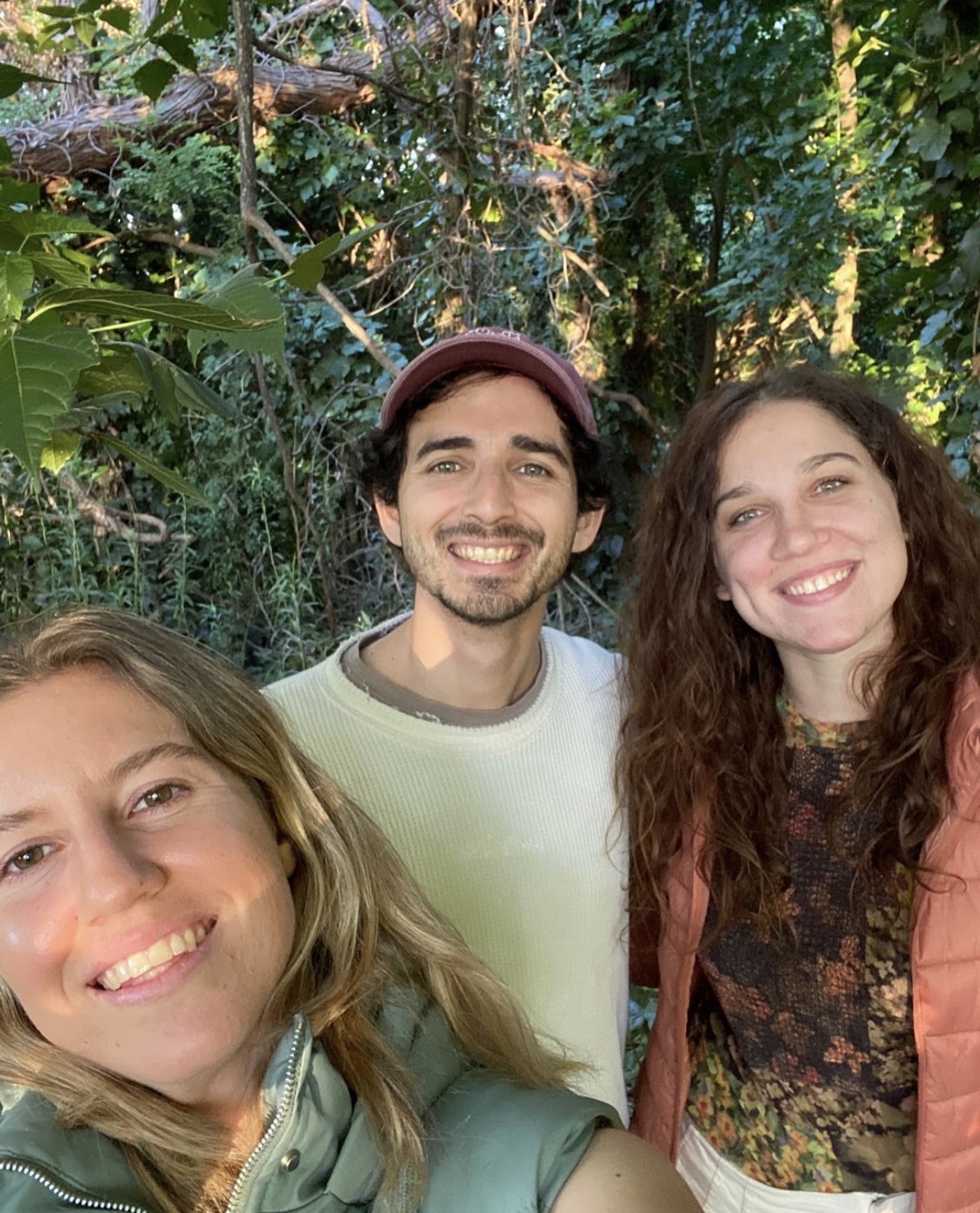 Mica, Alex, and a friend smiling outdoors among greenery